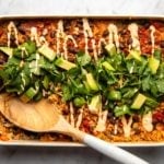 southwestern black bean casserole topped with cilantro and avocado in white baking dish on marble background