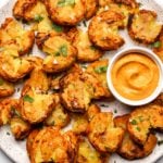white plate of smashed potatoes with parsley and side of romesco sauce
