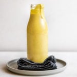 glass jar of curry tahini dressing on gray plate with navy napkin on white background