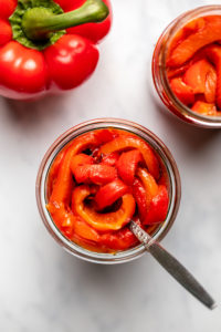 two glass jars of roasted red peppers with red pepper on marble background