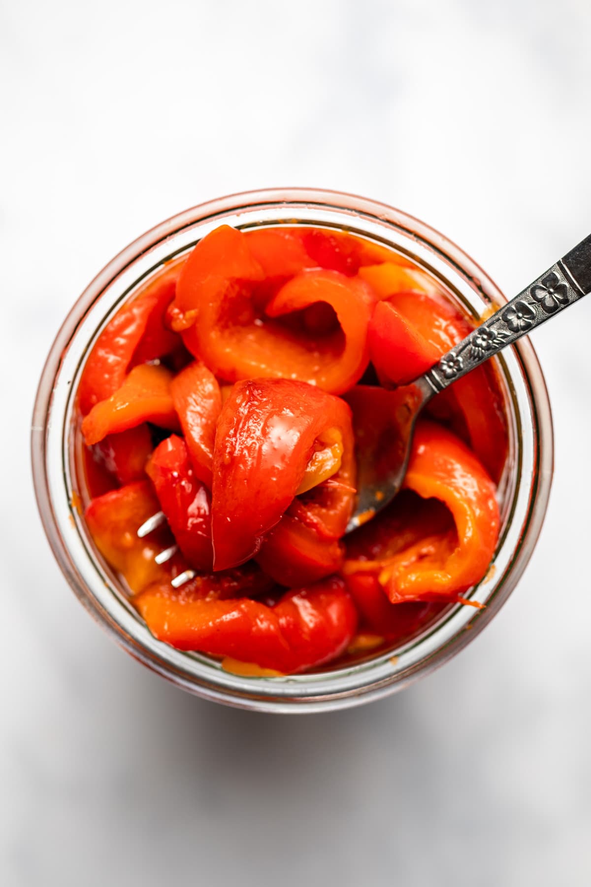 glass jar of roasted red peppers with silver fork on marble background