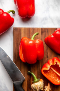 slicing bell peppers in half on wooden cutting board