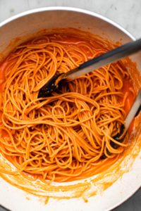 spaghetti noodles tossed with red pepper sauce in white pot