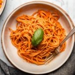 bowl of red pepper pasta topped with fresh basil on marble background