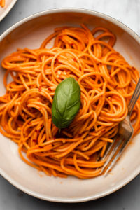 close up photo of spaghetti tossed in red pepper sauce topped with fresh basil