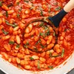 white pot of sweet & smoky white beans in red sauce garnished with chopped parsley
