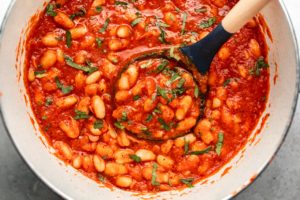 white pot of sweet & smoky white beans in red sauce garnished with chopped parsley