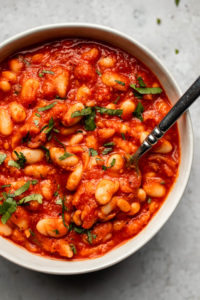 sweet and smoky white beans in red sauce in white bowl topped with parsley
