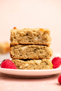 stack of vegan blondies on white plate with raspberries and pink background