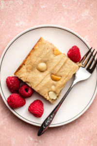 slice of vegan blondie on white plate with raspberries and fork