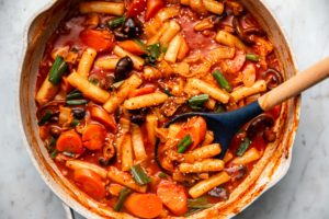pan of cooked tteokbokki with sesame seeds on marble background