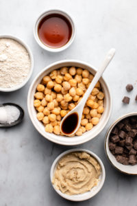 ingredients for chickpea chocolate chip cookies in small bowls on marble background