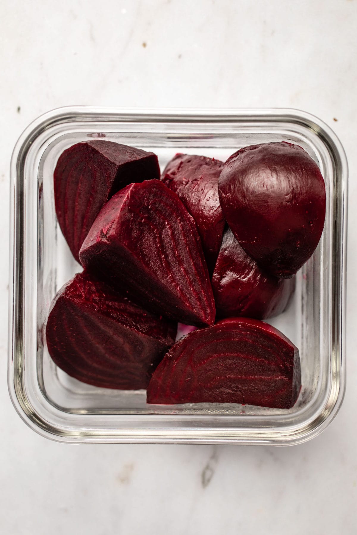 roasted quartered beets arranged in glass tupperware on marble background