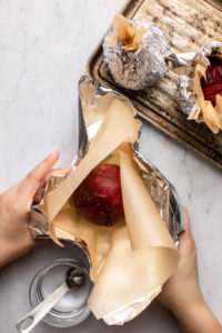 hands wrapping quartered beet in parchment paper and aluminum foil