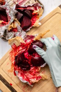 gloved hand peeling beets on wooden cutting board
