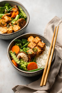 angled shot of peanut tempeh bowls with chopsticks on marble background