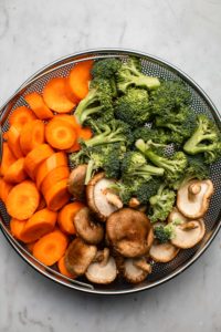 uncooked vegetables in steamer basket on white background