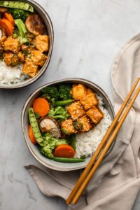 peanut tempeh bowls with steamed vegetables and rice on marble background