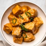 saucy peanut tempeh in white bowl topped with sesame seeds and sliced green onion