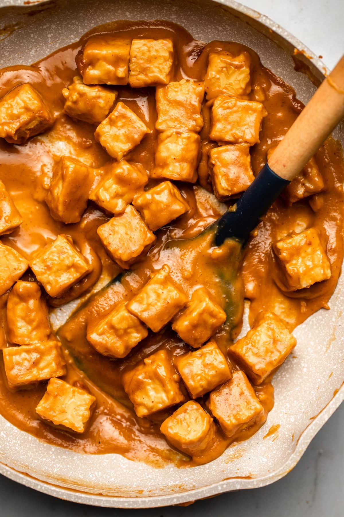 stovetop peanut tempeh cooked in white skillet with wooden spatula