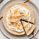 toasted coconut cheesecake on white speckled plate with slice taken out on marble background