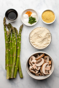 ingredients for asparagus mushroom quiche in small bowls on marble background
