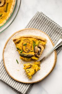 asparagus and mushroom quiche with bite taken out of it on speckled white plate