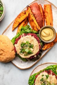 beet burger topped with hummus and greens on bun with sweet potato fries