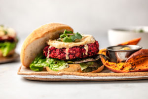 beet burger with lettuce and hummus on bun with sweet potato fries on marble background