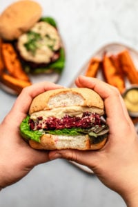 hands holding beet burger with bite taken out of it on marble background