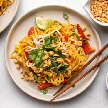 two plates of pad thai noodles on white plates with dishes of peanuts and lime wedges on the side