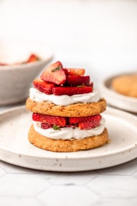 stack of strawberry shortcakes topped with strawberries and coconut cream on white plate with white background
