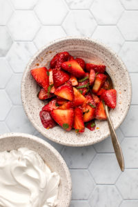 macerated strawberries in white bowl with bowl of coconut cream