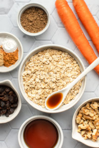 ingredients for carrot cake oatmeal in white bowls on tile background