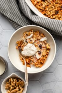 white bowl of carrot cake oatmeal topped with walnuts, coconut, coconut yogurt, and almond milk