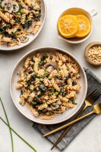 two bowls of lemon pasta with lemons, pine nuts, and chives on the side