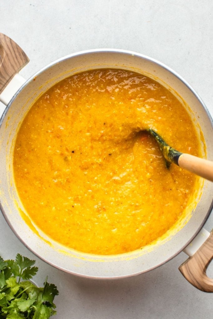stirring red lentil soup in white pot on grey background
