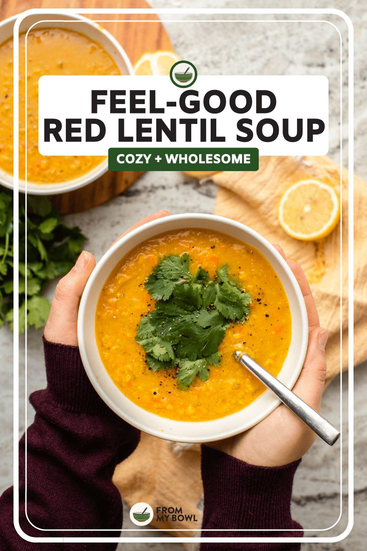 hands holding bowl of red lentil soup topped with cilantro