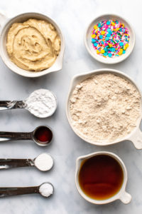 ingredients for funfetti cookies in small bowls on marble background