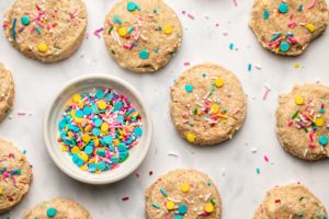 soft baked vegan funfetti cookies on marble background with small bowl of sprinkles