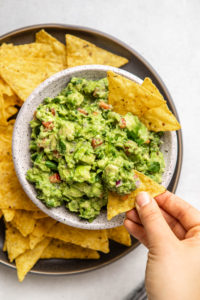 hand dunking tortilla chip into white bowl of guacamole