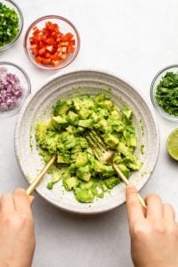 mashing chopped avocados with two forks in large bowl