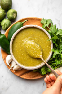 salsa verde in grey bowl with silver spoon on wood serving board