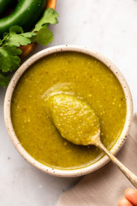 close up photo of spoon spooning salsa verde out of grey bowl