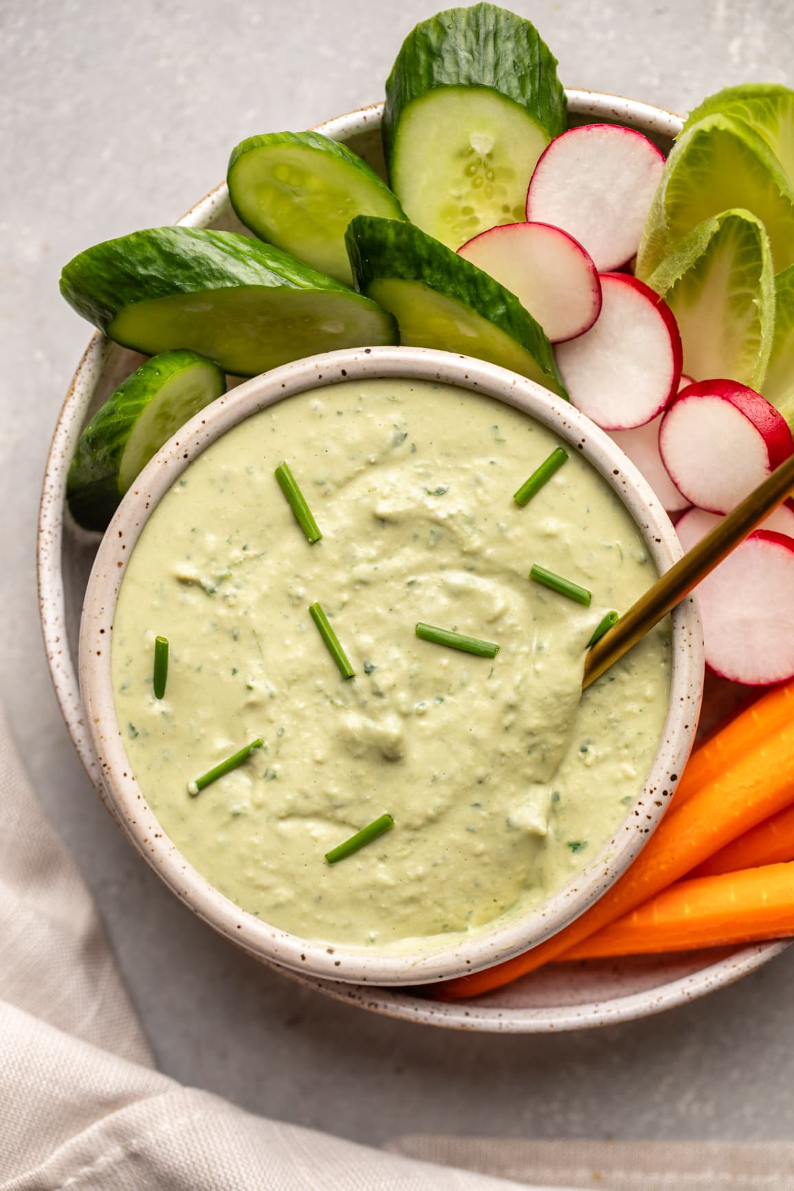 creamy white bean dip with herbs in grey bowl with cucumbers, radishes, and carrots