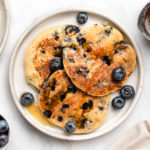 vegan blueberry pancakes on plate with maple syrup and fresh blueberries