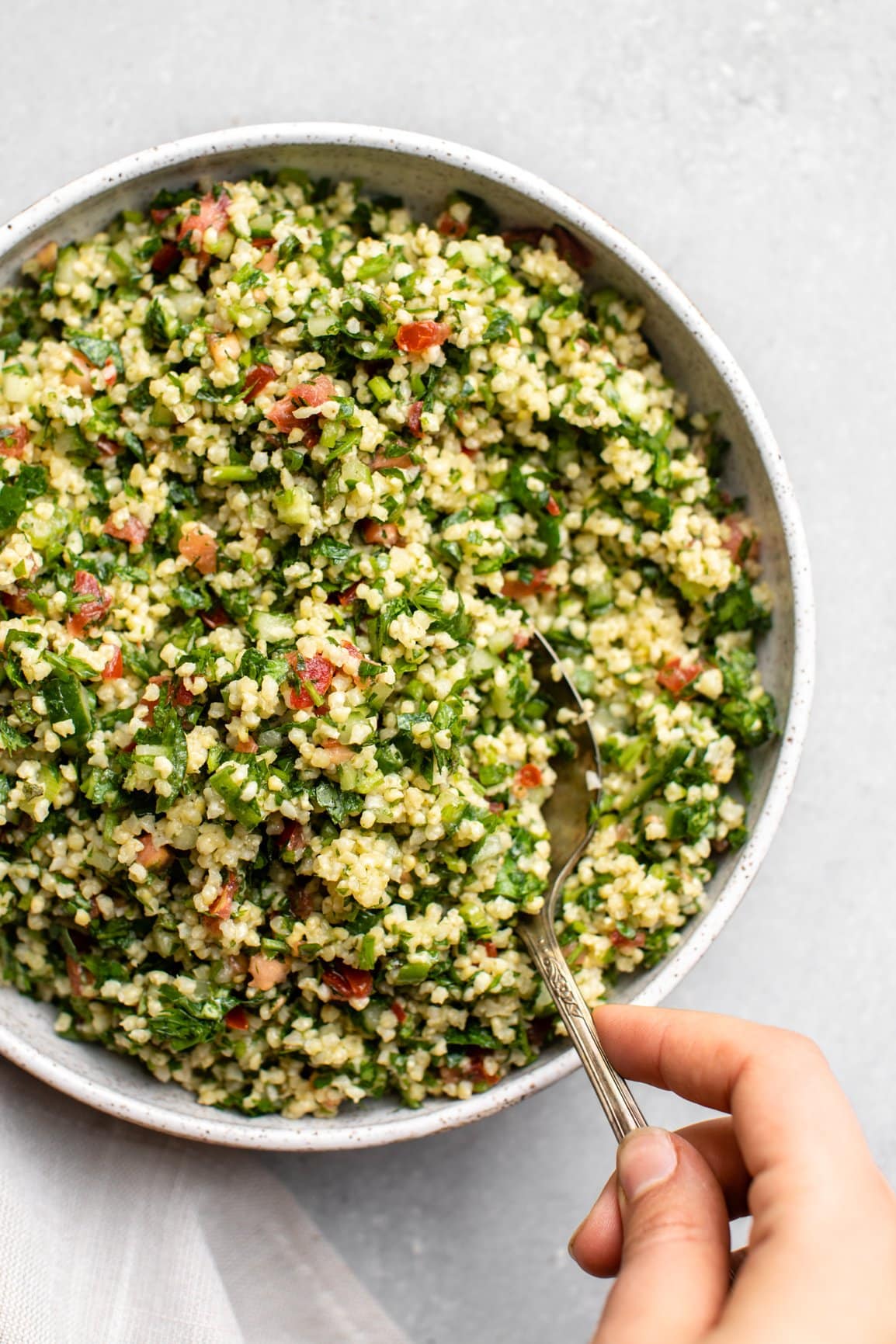 hand scooping spoonful of millet tabbouleh out of serving bowl