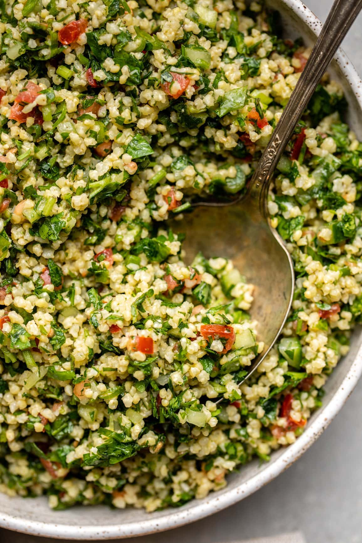 close up photo of millet tabbouleh in silver serving spoon in large bowl