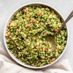 millet tabbouleh in white bowl with serving spoon on grey background