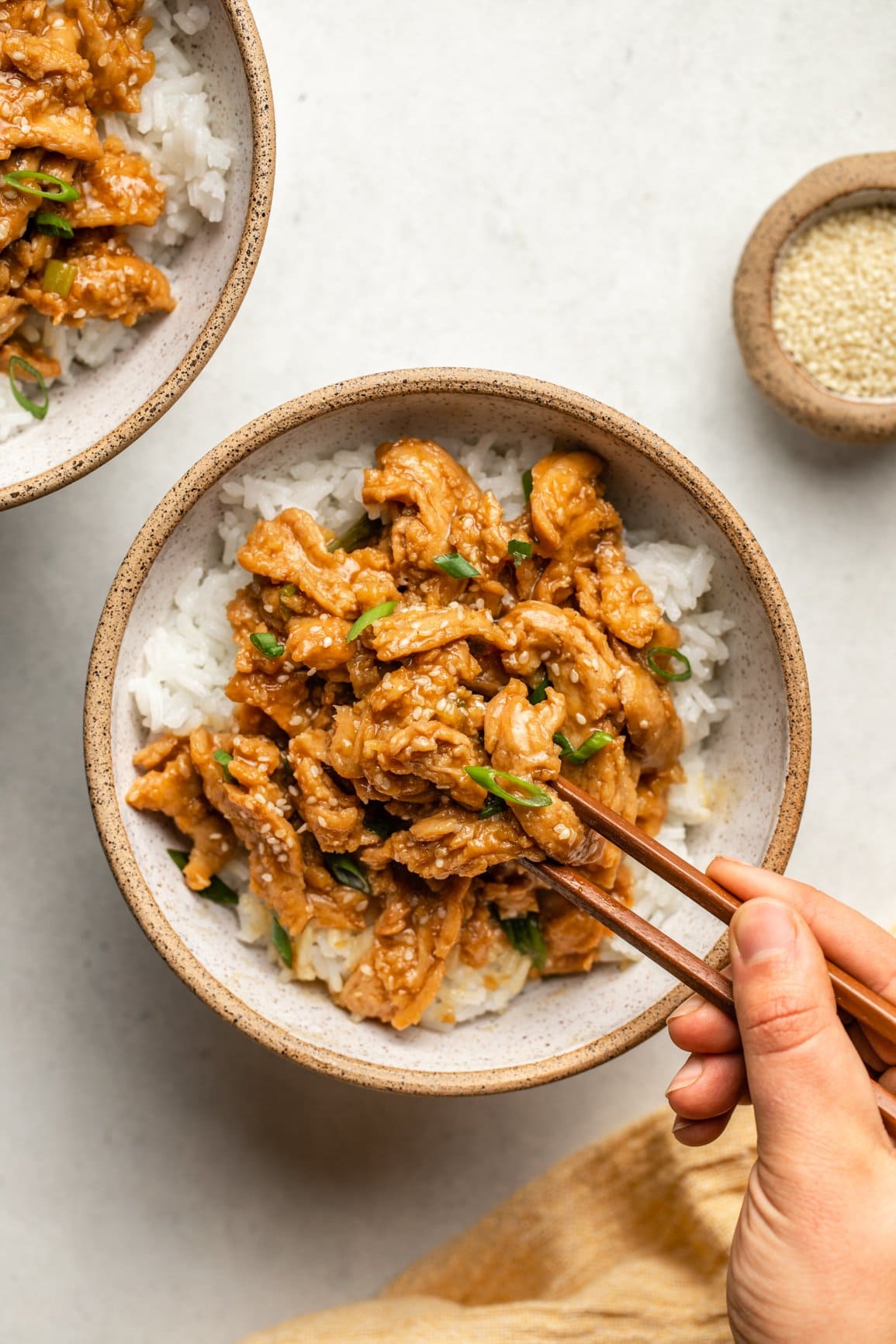 hands using chopsticks to take piece of vegan sesame chicken out of white bowl